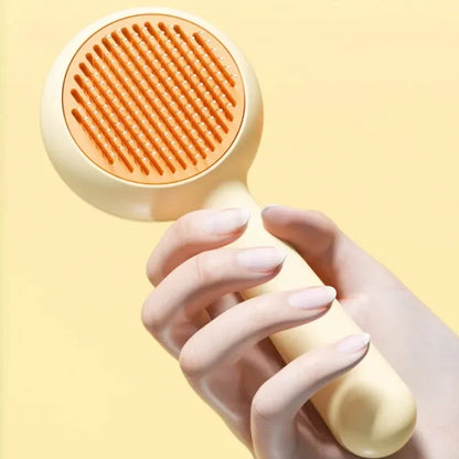 Hand holding a yellow pet grooming brush with orange bristles against a light background